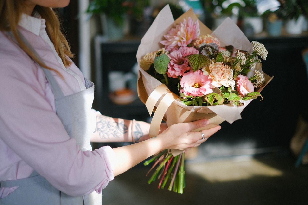 Close-up of a florist holding a colorful bouquet of flowers indoors, showcasing floral elegance.